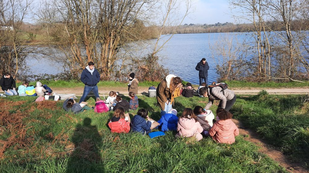 une classe d'enfants assis au bord d'un lac, ils remplissent chcun un formulaire pour décrire une petite bête rencontrée au cours de la sortie