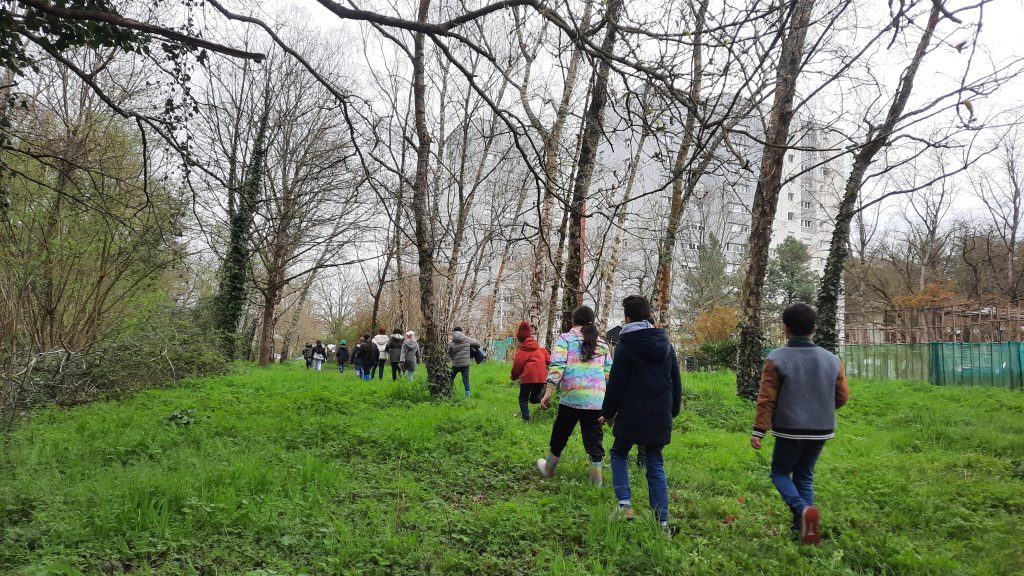 une classe se dirige à la queue leu leu entre les arbres vers la cité où se trouvent leur école